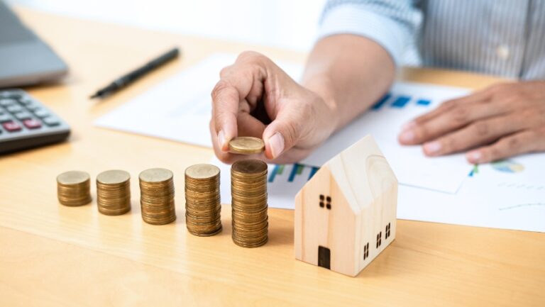 Personne consultant un plan d’investissement immobilier, ordinateur affichant des graphiques financiers et photo d’immeuble