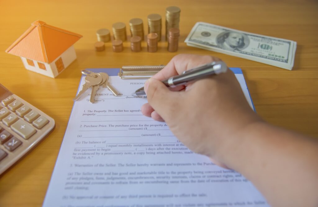 Une personne écrit sur un papier avec une clé de maison, des argents et une calculatrice