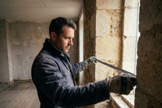Artisan mesurant l'ouverture d'une fenêtre en pierre avant pose au Mans